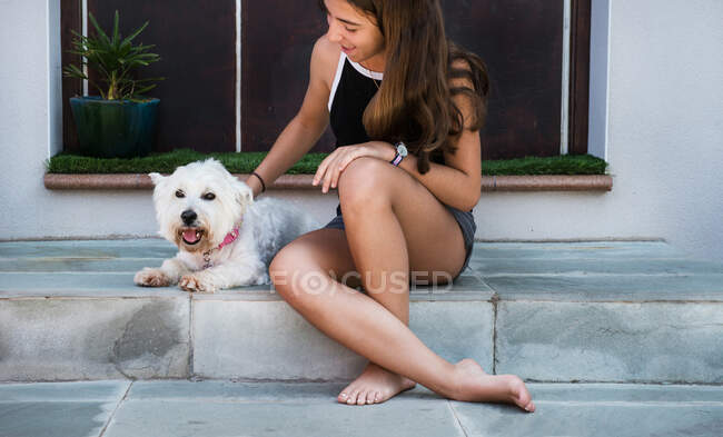Adolescente chica sentado en patio escalera acariciar perro - foto de stock
