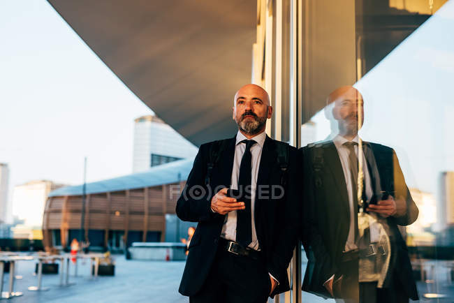 Mature businessman leaning against window outdoor — Stock Photo