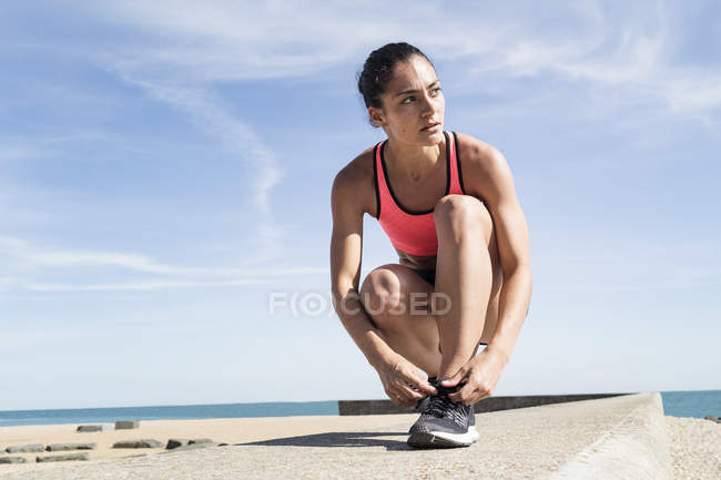 Jeune femme sur le mur de la mer attachant lacet — Photo de stock