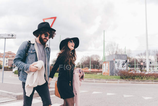Young couple outdoors, crossing road, holding hands, laughing — Stock Photo