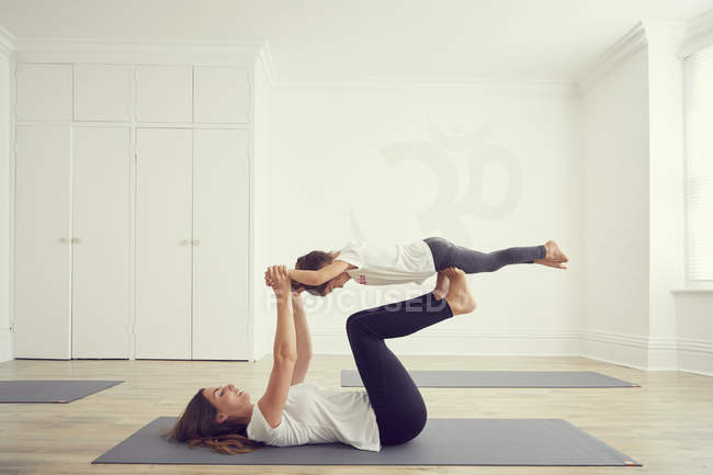 Mother and daughter in yoga studio, daughter balancing on mothers legs — Stock Photo