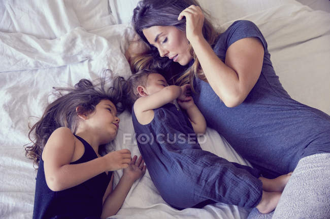 Madre y dos niños pequeños, acostados en la cama - foto de stock