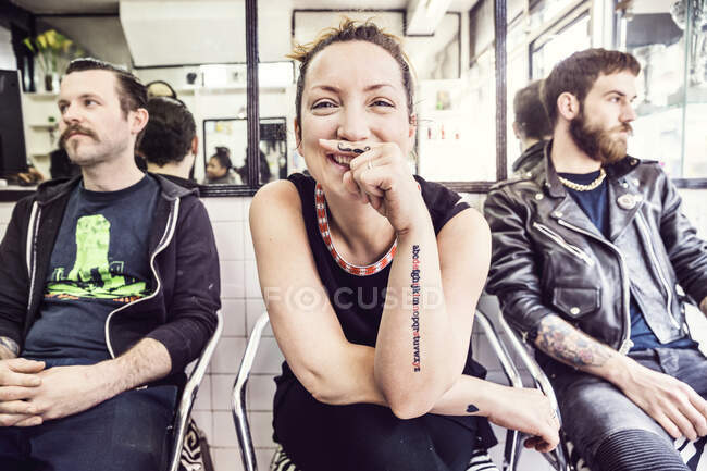 Frau mit Schnurrbart-Tätowierung am Finger blickt lächelnd in die Kamera — Stockfoto