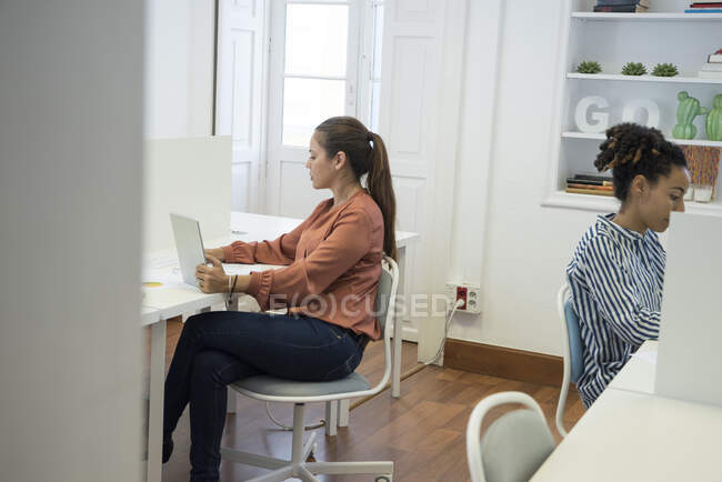 Dos mujeres de negocios escribiendo en computadoras portátiles en el escritorio de la oficina - foto de stock