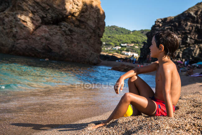 Мальчик, сидящий на пляже с видом на море, Бегур, Каталония, Испания — стоковое фото