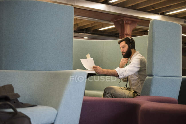 Вид збоку чоловіка в кабінці в навушниках, що дивляться на паперові роботи — стокове фото