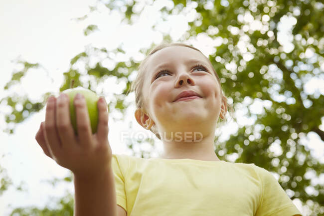Junges Mädchen, im Freien, mit Apfel in der Hand, Blick in den niedrigen Winkel — Stockfoto