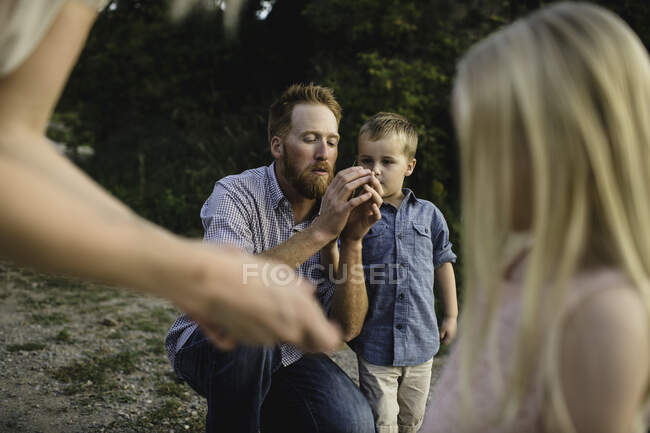 Padre mostrando a hijo cómo silbar con hierba - foto de stock