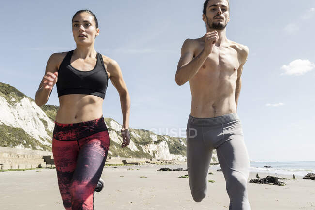 Jovem e mulher correndo ao longo da praia, vista frontal — Fotografia de Stock