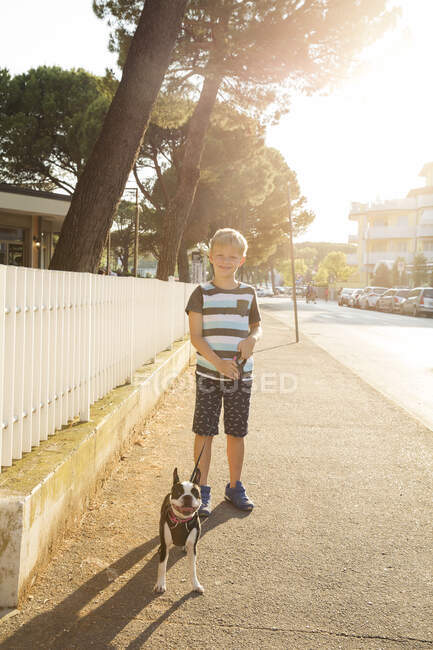 Retrato de niño con perro en la calle mirando a la cámara sonriendo - foto de stock