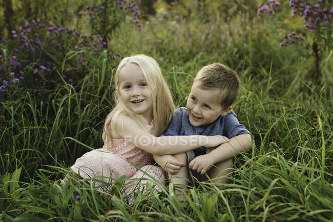 Junge und Mädchen sitzen zusammen im hohen Gras — Stockfoto