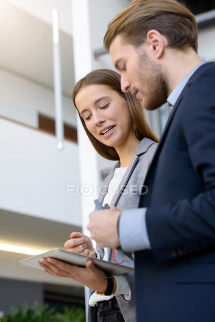 Jeune femme d'affaires et homme utilisant une tablette numérique dans l'atrium de bureau — Photo de stock