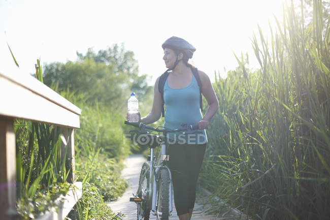 Cyclist walking with bike on path through tall grass — Stock Photo