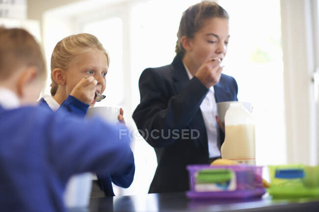 Девочка-подросток с сестрой и братом, кушающая хлопья на кухне — стоковое фото