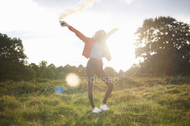 Young woman letting off smoke flare in sunlit field — Stock Photo