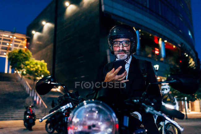 Mature businessman sitting on motorcycle with smartphone — Stock Photo