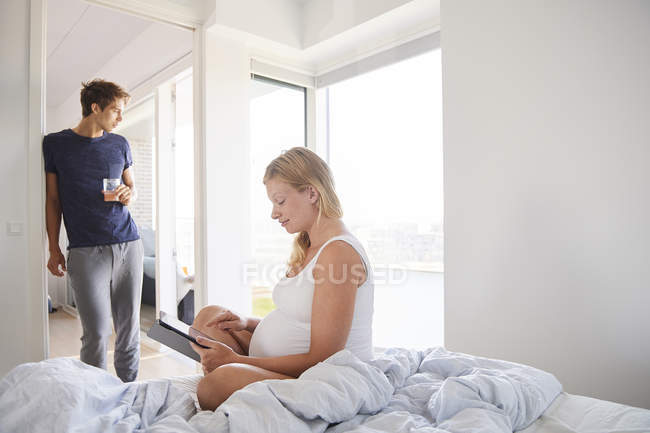 Schwangere junge Frau nutzt digitales Tablet im Bett — Stockfoto