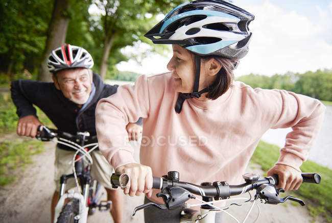 Mature couple cycling on pathway beside lake — Stock Photo