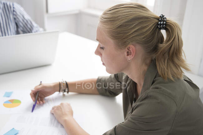 Joven empresaria haciendo notas sobre papeleo en el escritorio de la oficina - foto de stock