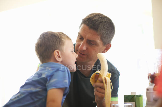 Niño y padre compartiendo plátano fresco en la cocina - foto de stock