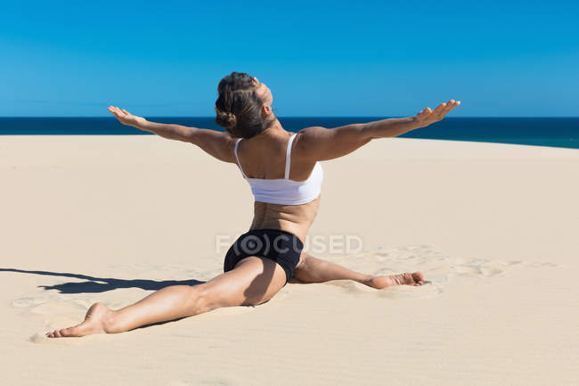 Vue arrière de la femme sur la plage en position de yoga — Photo de stock