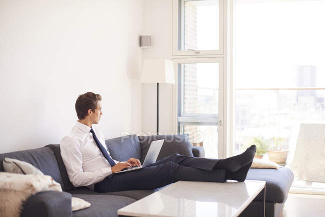 Uomo d'affari che utilizza laptop sul divano in soggiorno — Foto stock