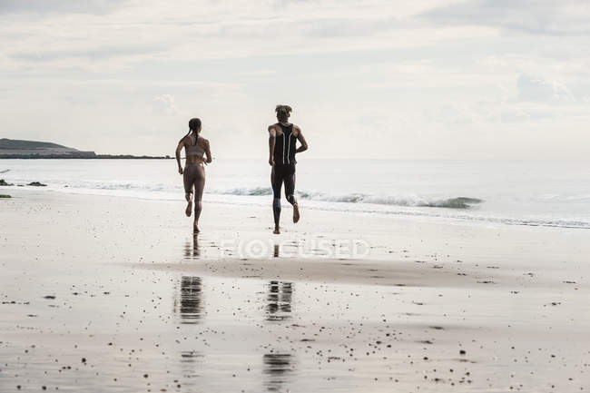 Vue arrière de jeunes hommes et femmes courant pieds nus le long de la plage — Photo de stock
