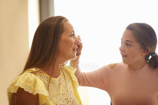 Young girl drawing on mother's face, using face paint — Stock Photo