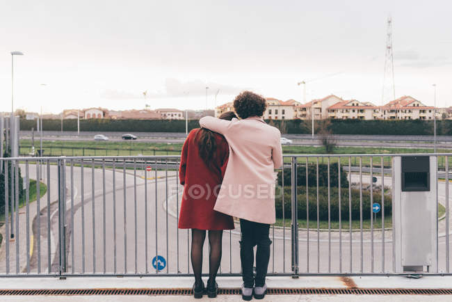 Молодая пара стоит на пешеходном мосту, смотрит на вид, вид сзади — стоковое фото