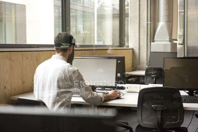 Vue arrière de l'homme au bureau en utilisant un ordinateur de bureau — Photo de stock