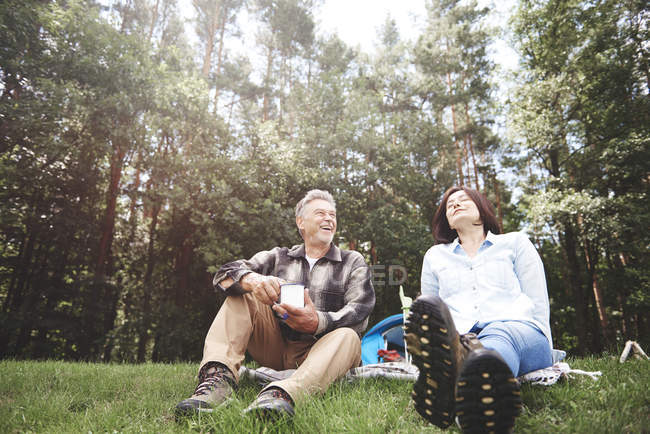 Mature couple relaxing on grass with forest at background — Stock Photo