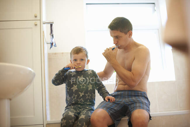 Niño en el baño con el padre cepillándose los dientes juntos - foto de stock