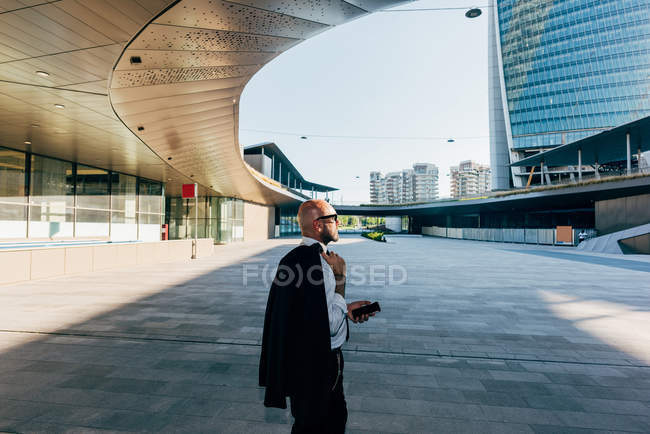 Mature businessman walking outdoors with suit jacket over shoulder — Stock Photo