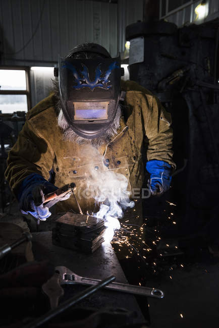 Schmied in Schweißmaske schweißt Metall in Werkstatt — Stockfoto