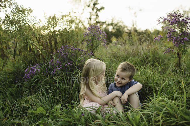 Menino e menina sentados na grama alta juntos — Fotografia de Stock