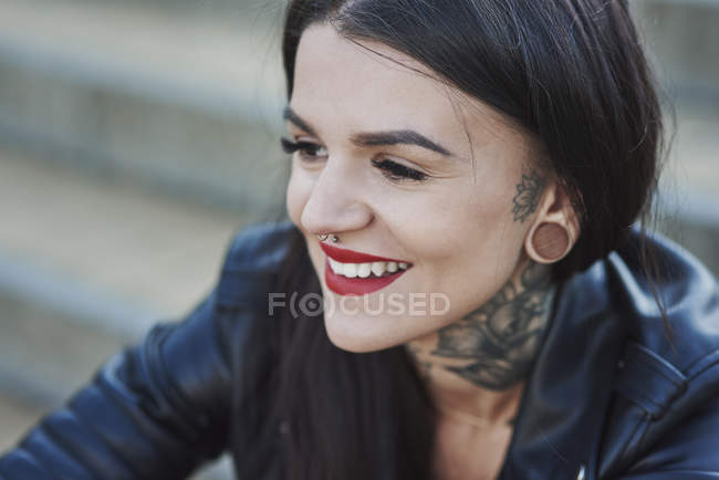 Retrato de mulher jovem sorrindo, tatuagens no pescoço, nariz e piercings na orelha, close-up — Fotografia de Stock