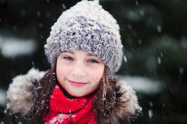 Portrait of girl in falling snow smiling at camera — Stock Photo