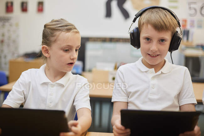 Schoolboy listening to headphones in class at primary school, portrait — Stock Photo
