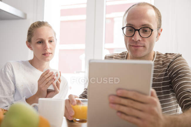 Jeune femme et petit ami regardant sur tablette numérique à la table du petit déjeuner — Photo de stock