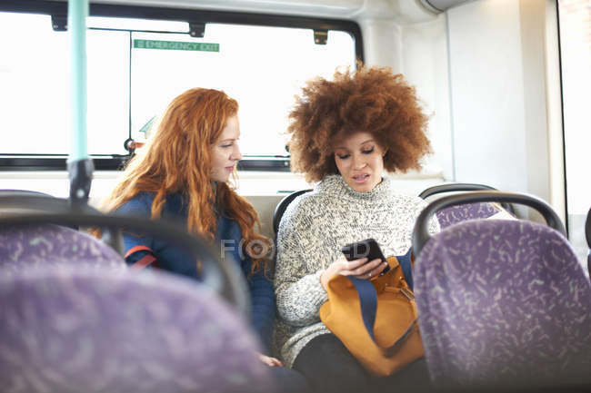 Две молодые женщины в автобусе смотрят на смартфон — стоковое фото