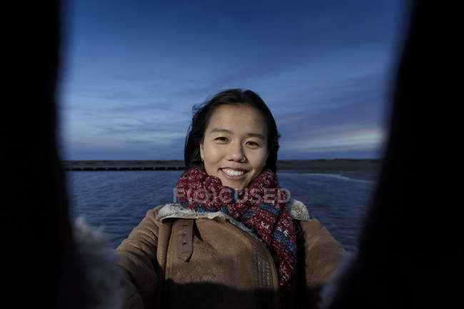 Portrait of young woman taking selfie on beach at dusk — Stock Photo