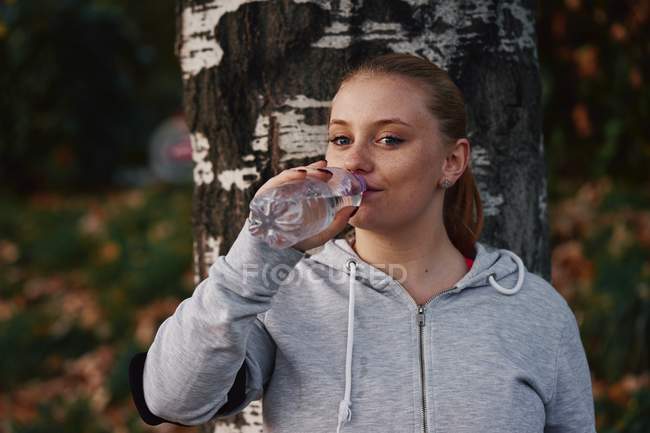 Porträt einer jungen Frau, die im Park Mineralwasser trinkt — Stockfoto