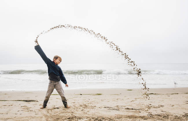 Портрет молодого хлопчика на пляжі, що кидає пісок у формі арки — стокове фото