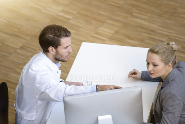 Male doctor and young woman sitting at table, looking at computer screen — Stock Photo