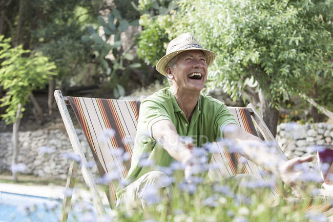 Homem no jardim sentado na cadeira do convés rindo — Fotografia de Stock