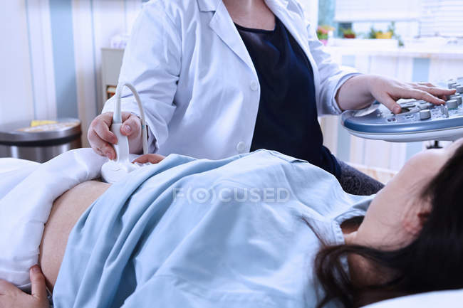 Vista ritagliata del sonografo che esegue la scansione ecografica della paziente incinta — Foto stock