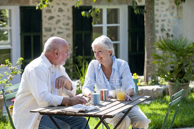 Старшая пара сидит в саду, чашки кофе на столе — стоковое фото