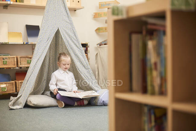 Школярка сидить на підлозі читання в класі в початковій школі — стокове фото