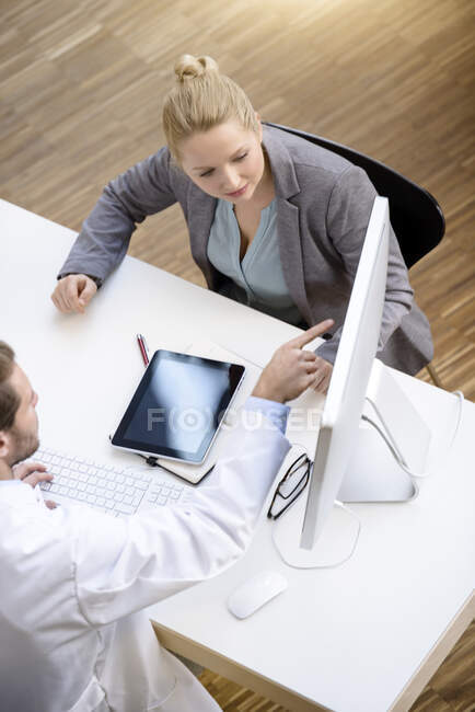 Männlicher Arzt und junge Frau sitzen am Tisch und schauen auf den Computerbildschirm — Stockfoto