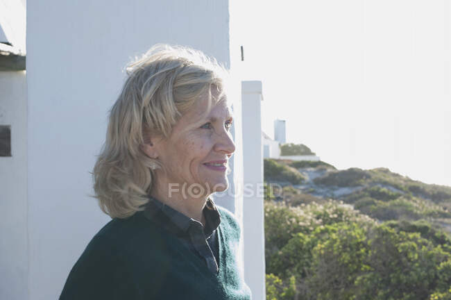 Happy blond haired senior woman looking out from sunlit coastal home, Cape Town, Western Cape, South Africa — Stock Photo